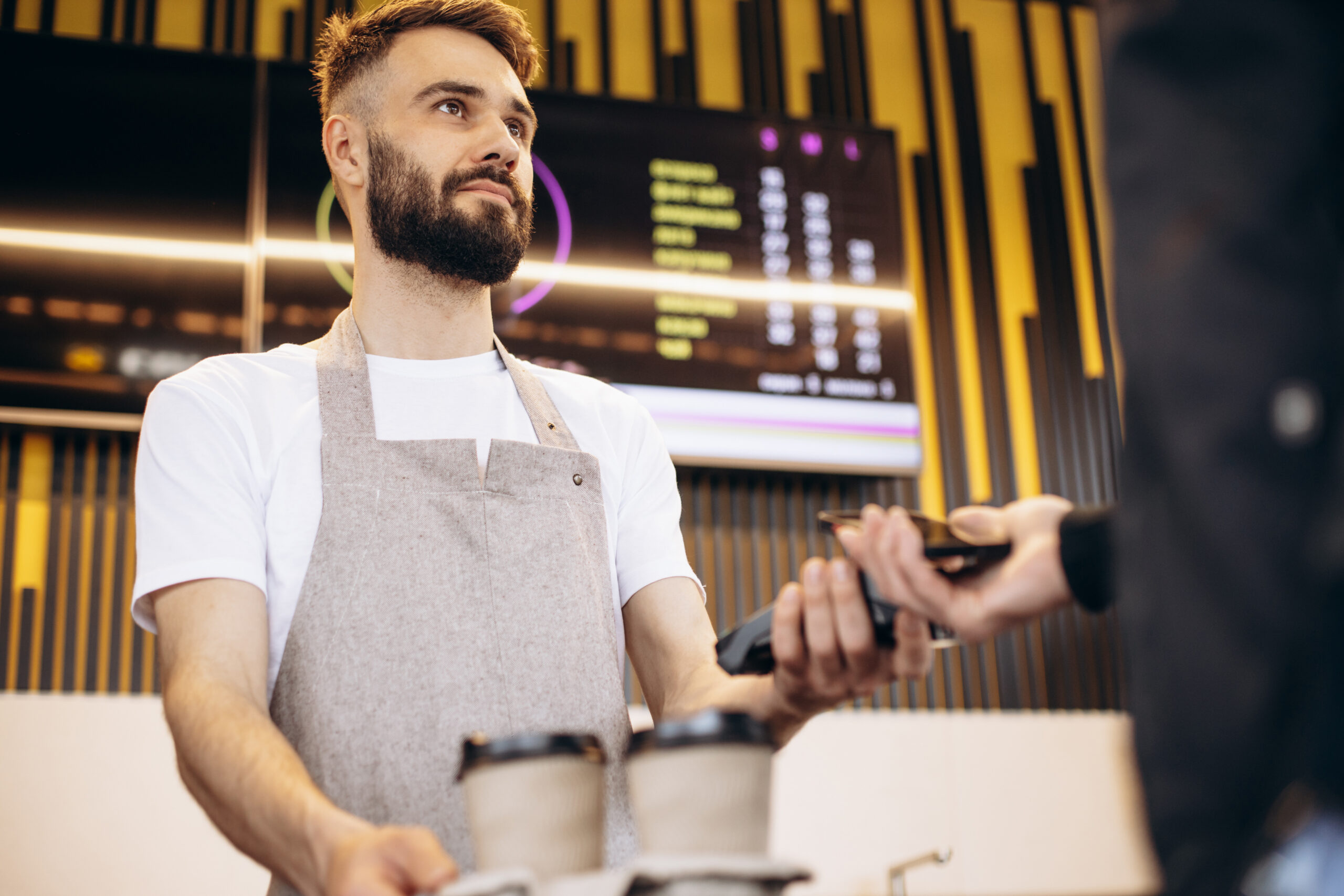 Male barista holding terminal while customer paying with card